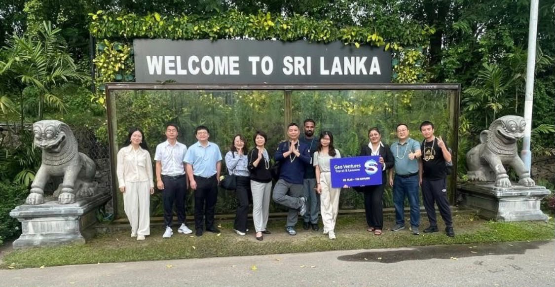 Tour group holding a Geo Ventures sign under the Welcome to Sri Lanka sign