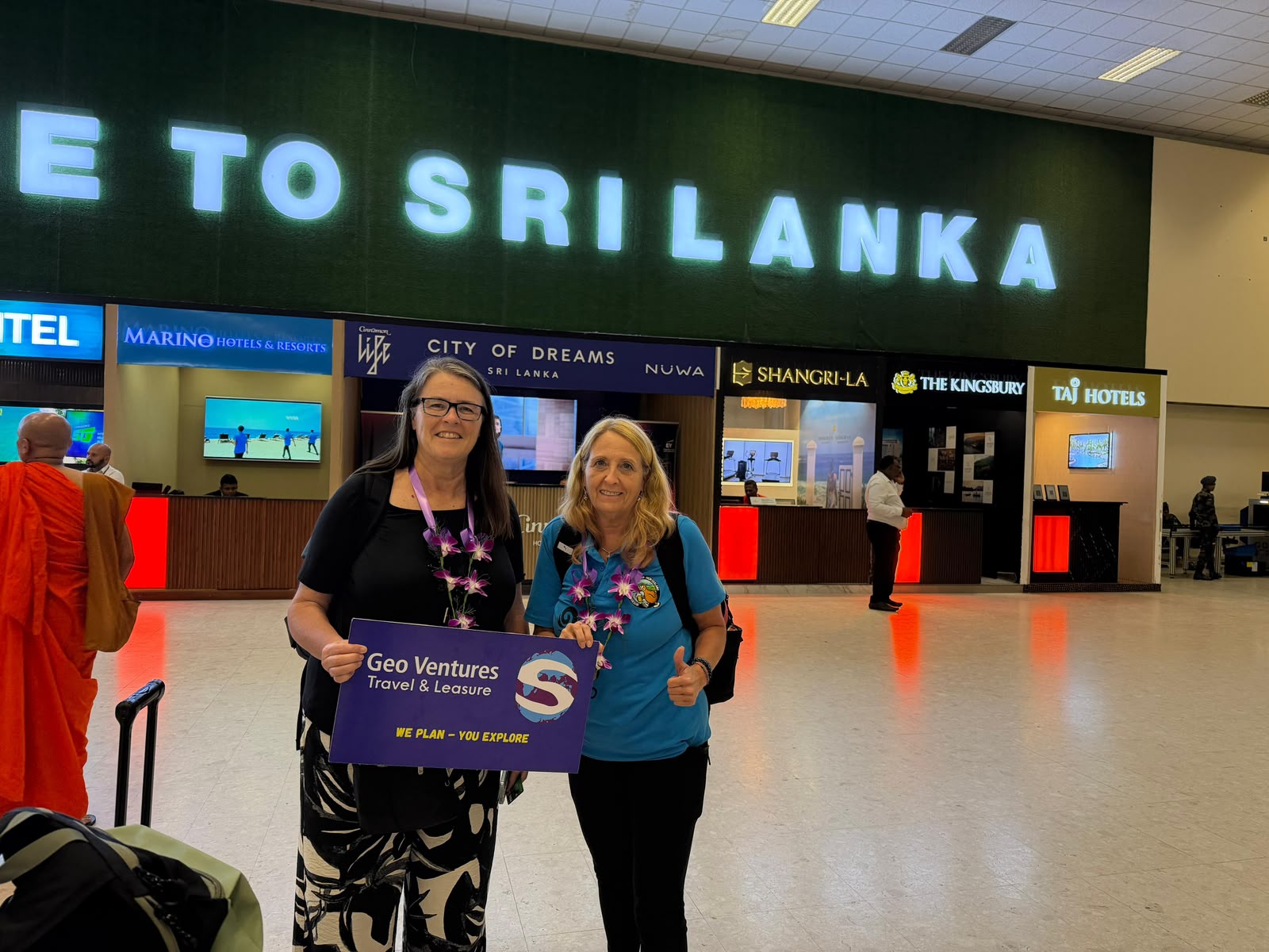 Two travellers with orchid garlands holding a Geo Ventures sign at the airport