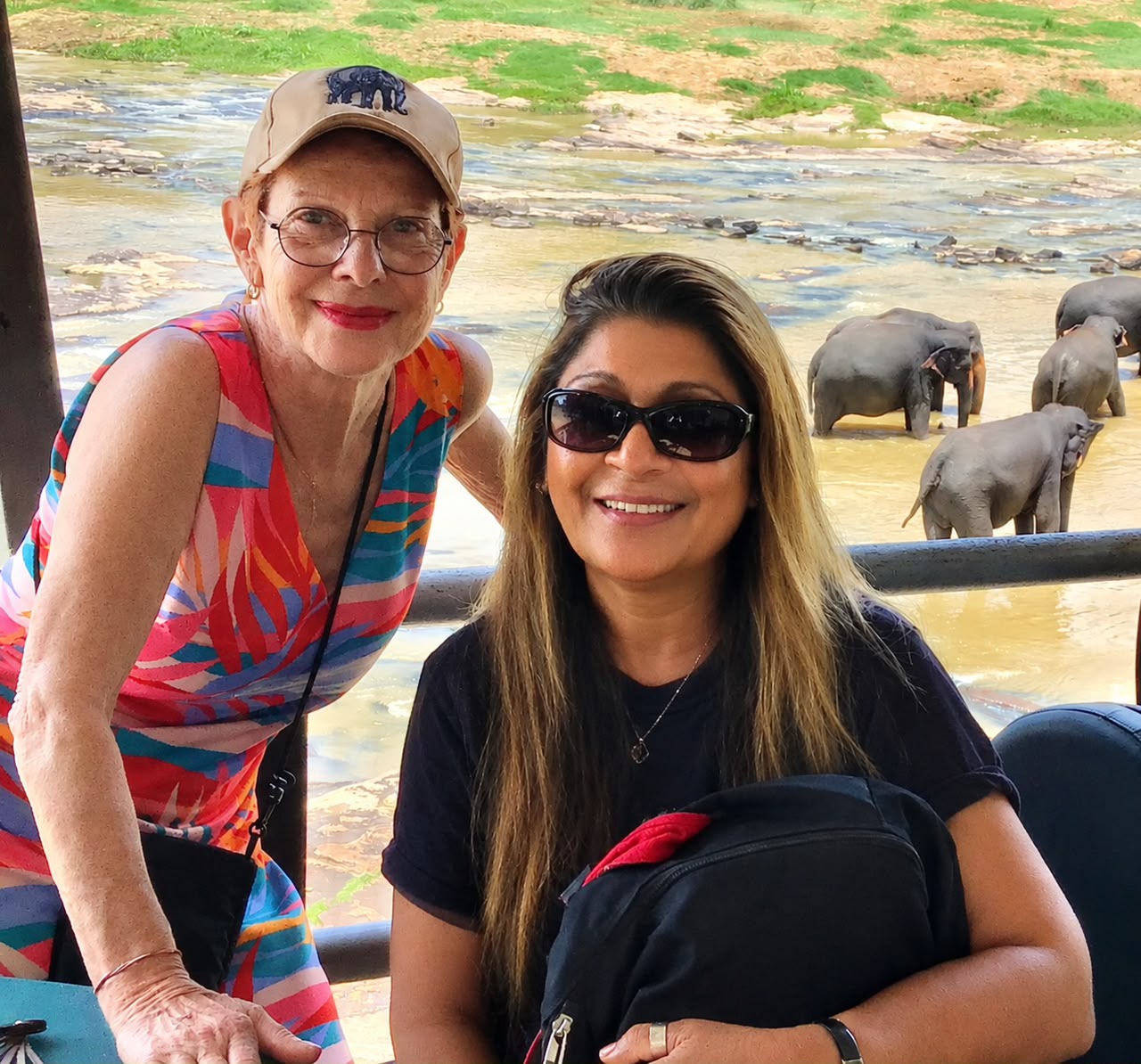 Guests smiling by the river as a herd of elephants bathes behind them